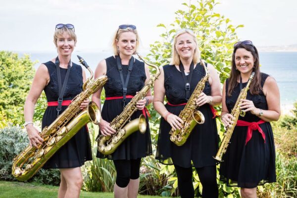 Four ladies stand in a line, dressed in black, holding their saxophones.