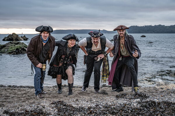 Four pirates standing on a beach withsea and cliffs in the background