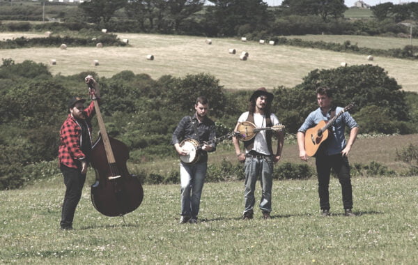 The band stand with their instruments in a field.